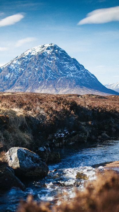 Person sat beside a stream enjoying mountain view in Glencoe, Scotland