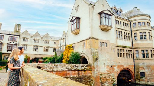 Young couple stood on stone bridge looking at country house