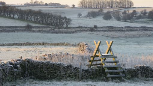Wooden stile over drystone wall amongst fields. Winter frost in Bristol, Somerset, England