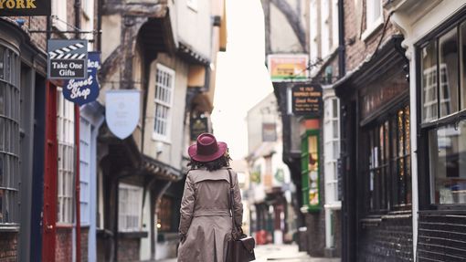 Woman wearing trench coat and pink hat walking through narrow historic street of York, North Yorkshire, England. 