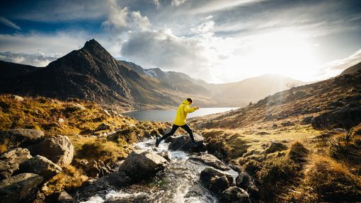A man jumping across a stream whilst hiking