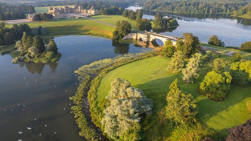 An aerial view of a serene lake with the majestic Blenheim Palace residence nestled on its shores.