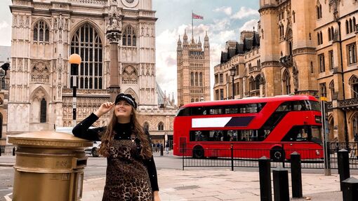 Girl standing next to a golden letter box with a red London bus and Westminster Abbey facade in the background