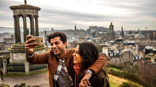 Couple taking a selfie on a mobile phone with Edinburgh in the background