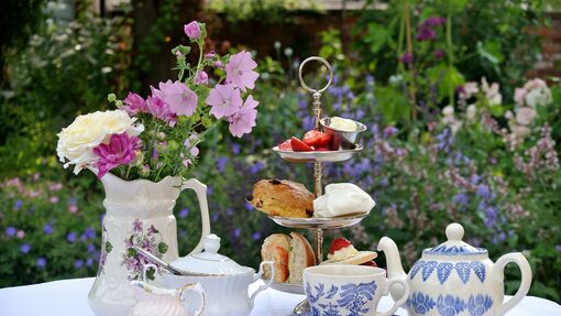  Cakestand full of sandwiches and cakes with a pot of tea on a table in a garden