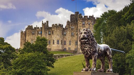 An historic castle with a UK flag at full mast and with a lion statue out the front
