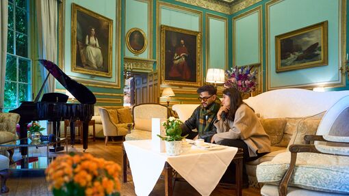 A man and woman having tea in a room with antique paintings and furniture