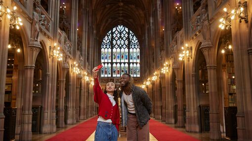 Two people walking through a dramatically lit library in Manchester