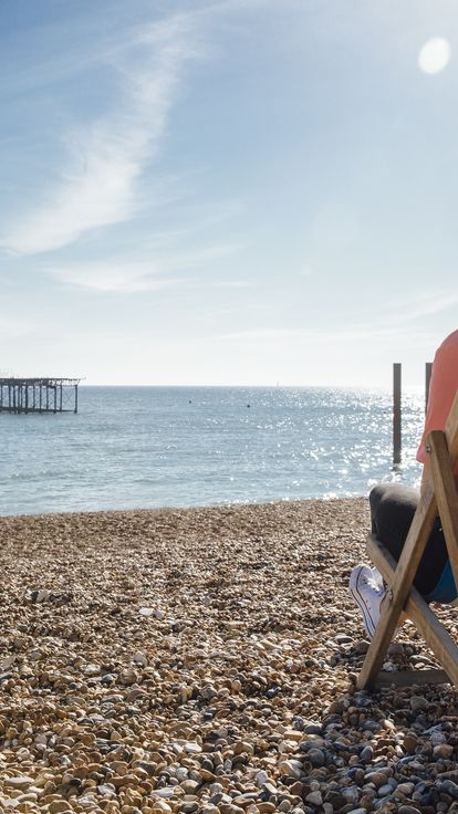 Rear view of woman sitting in striped deckchair on the beach