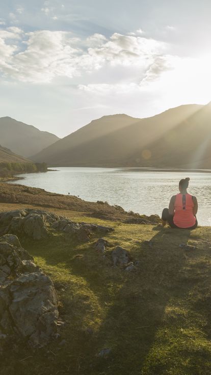 Woman, meditating in green valleys, near lake. High sun