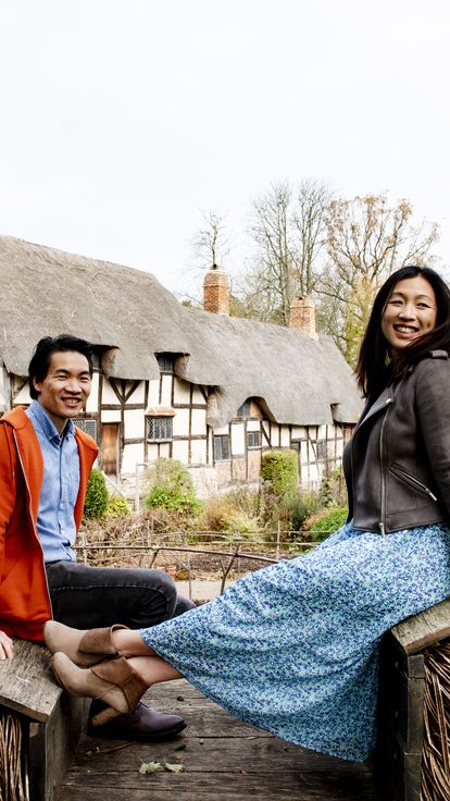 Asian couple sitting on a wooden sculpture in Stratford-upon-Avon with Shakespeare's birthplace in the backdrop