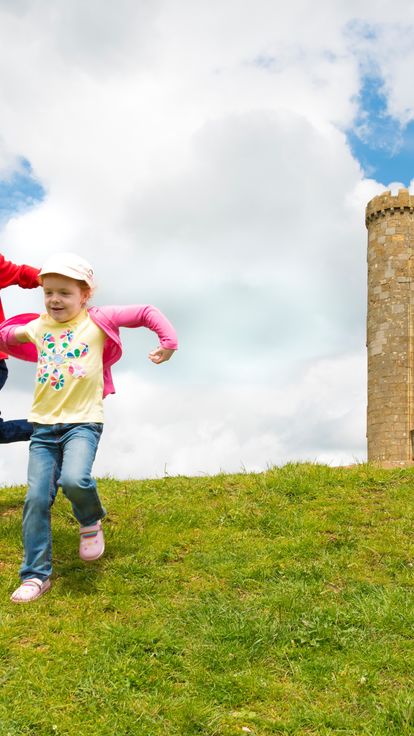 Two children running down a hill near a stone tower