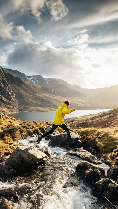 A man jumping across a stream whilst hiking