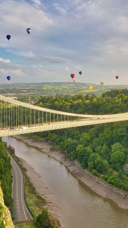 Aerial view of a large suspension bridge with hot air balloons taking to the air