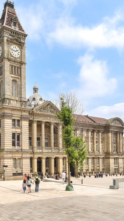A square in Birmingham with crowds walking past ornate city buildings