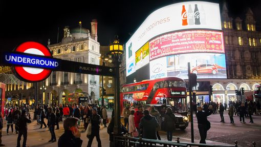 view of the crowded Piccadilly Circus at night time with the large led screens in the distance and the London underground sign at the front