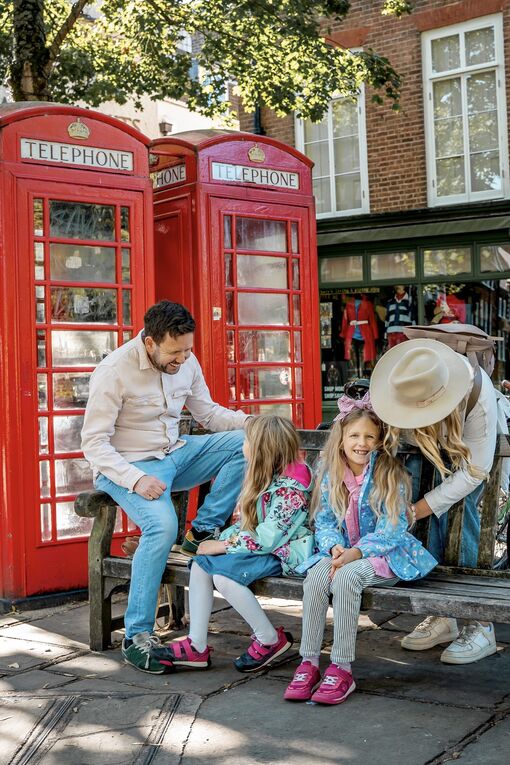 A family of four sitting by two iconic red telephone boxes in London