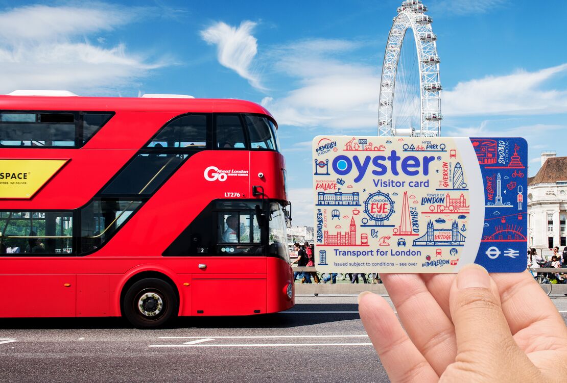 A tourist holding a Visitor Oyster card by a red London bus