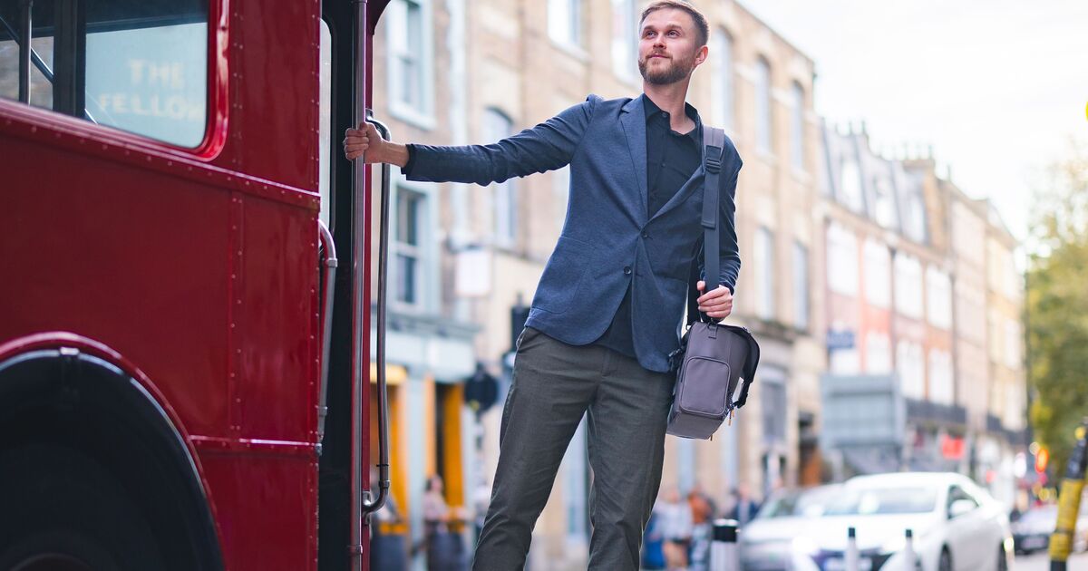 A man stands at the end of a red bus in London