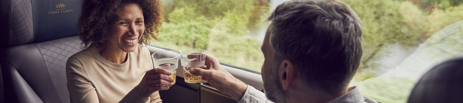 A couple enjoying a drink while travelling by train from Bath, sitting at a table,