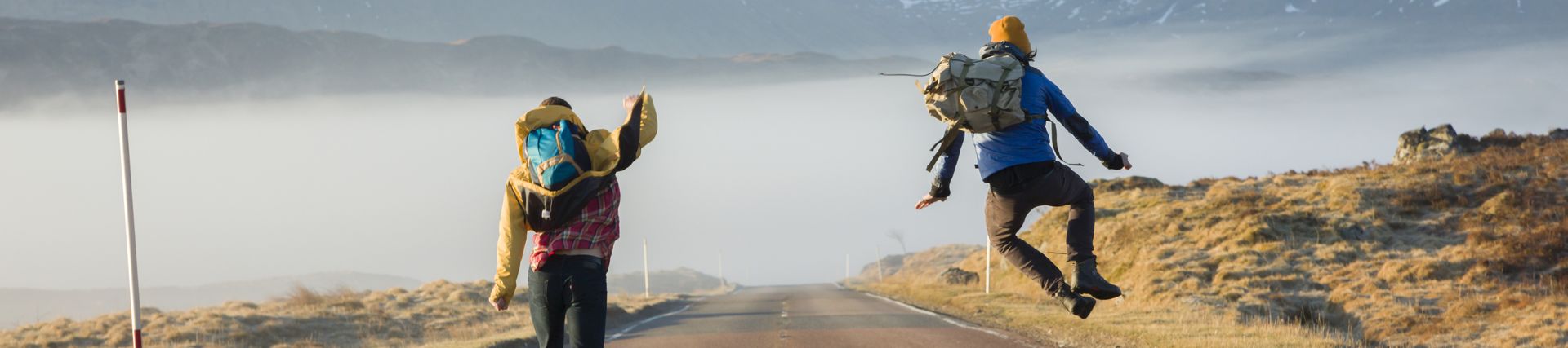 Rear view of two men jumping with joy on a country road