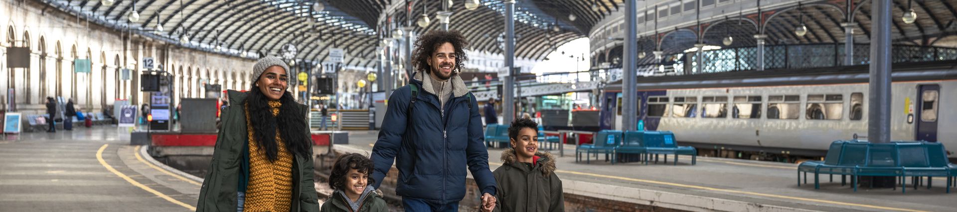 A multi-racial family of four, a mother, father and their two little boys walking