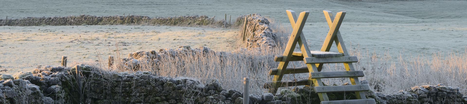 Wooden stile over drystone wall amongst fields. Winter frost in Bristol, Somerset, England