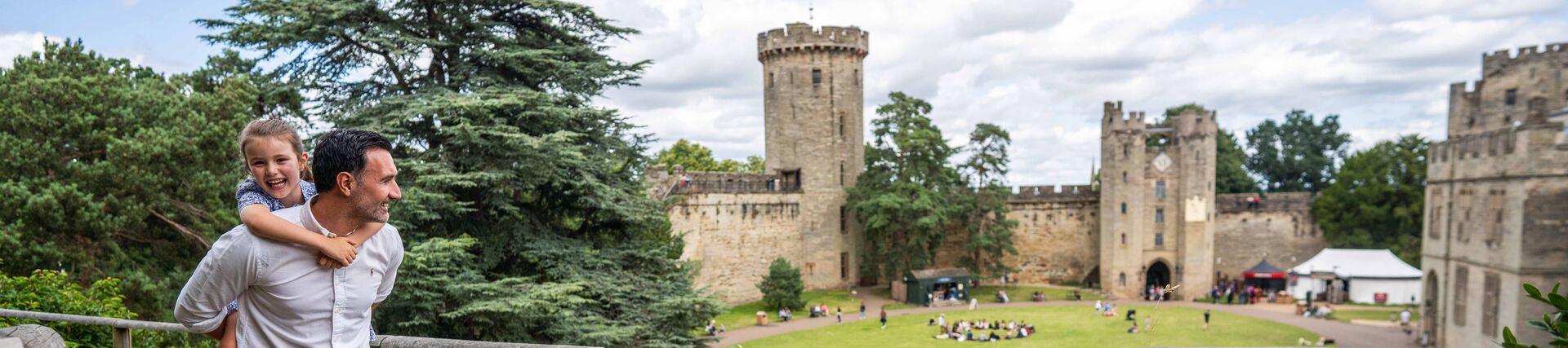 Father carrying his daughter, smiling and exploring the grounds of a castle