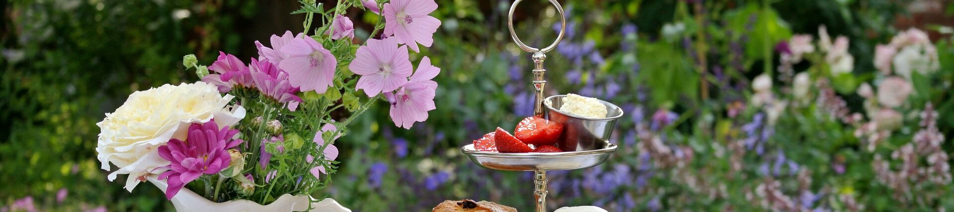  Cakestand full of sandwiches and cakes with a pot of tea on a table in a garden