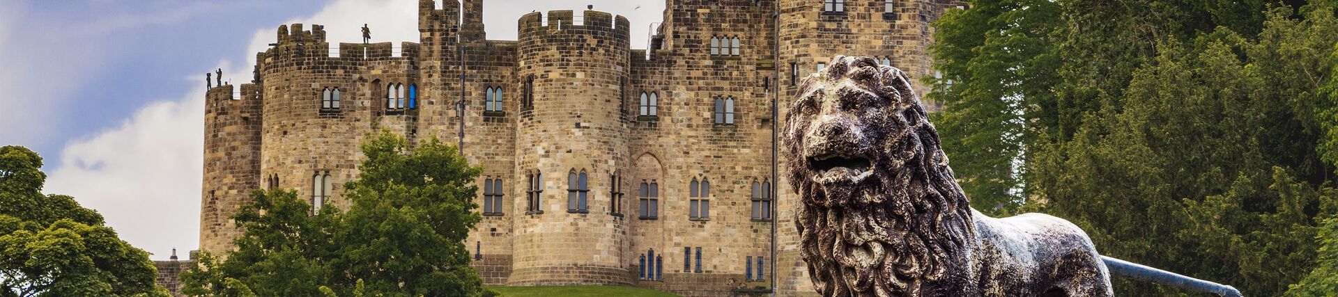 An historic castle with a UK flag at full mast and with a lion statue out the front