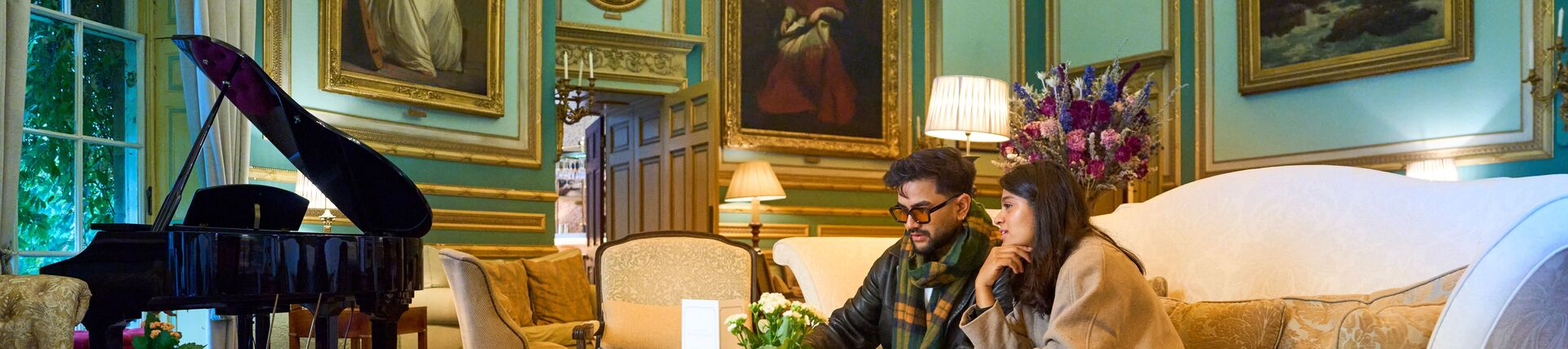 A man and woman having tea in a room with antique paintings and furniture