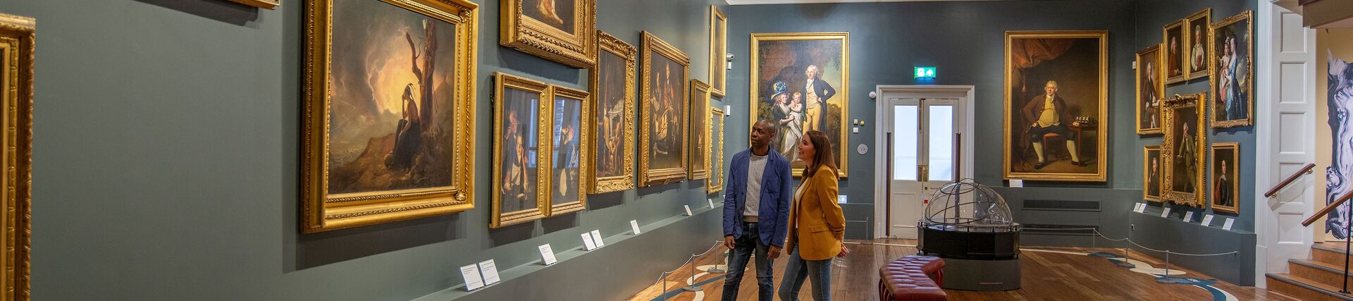 A man and a woman stand looking at paintings in a gallery