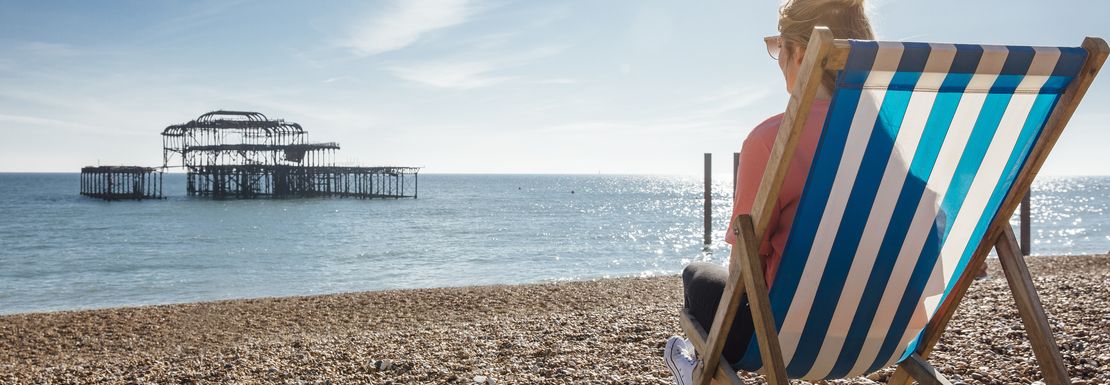 Rear view of woman sitting in striped deckchair on the beach