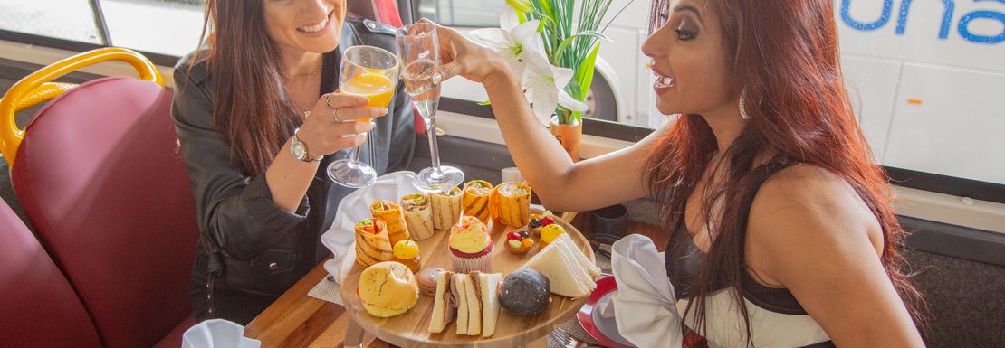 Two visitors tasting a triple deck tray with scones, sandwiches and cakes on the The English Tea Bus at the Golden Tour's Panoramic Tour of London
