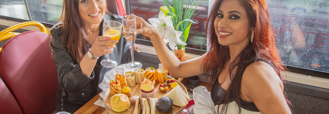 Two visitors tasting a triple deck tray with scones, sandwiches and cakes on the The English Tea Bus at the Golden Tour's Panoramic Tour of London
