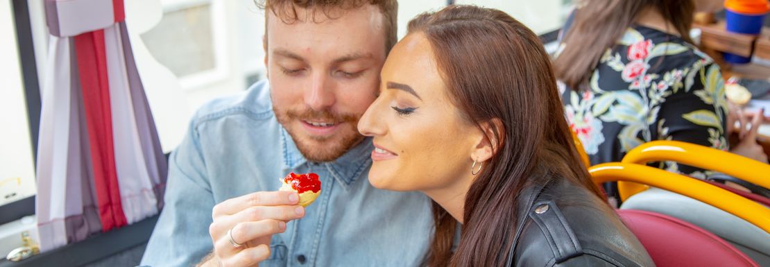 A couple tasting a triple deck tray with scones, sandwiches and cakes on the The English Tea Bus at the Golden Tour's Panoramic Tour of London