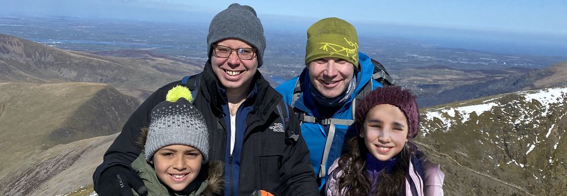 A family including two children climbs up Mount Snowdon and smiles