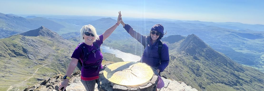 Two hikers high five as they reach the top of Snowdonia on a beautiful day