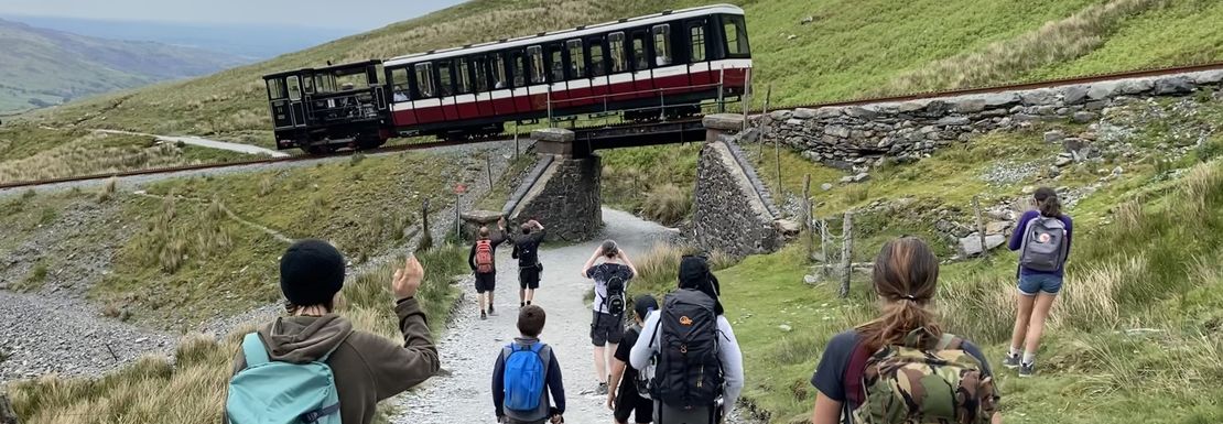 A small train passes overhead as climbers enjoy the sight up on Mount Snowdon