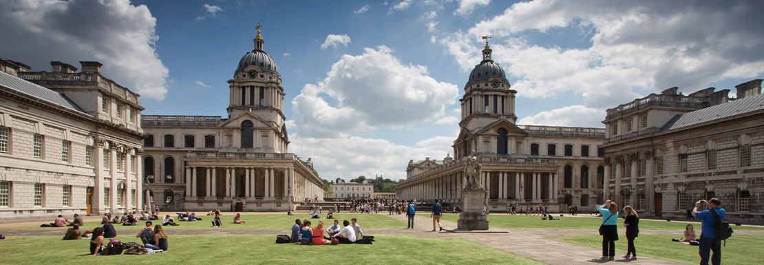 People relax outside on the lawn of the Old Royal Naval College