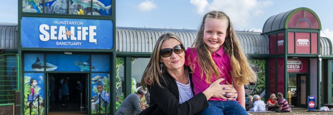 A mum and daughter sit together outside the entrance to the aquarium