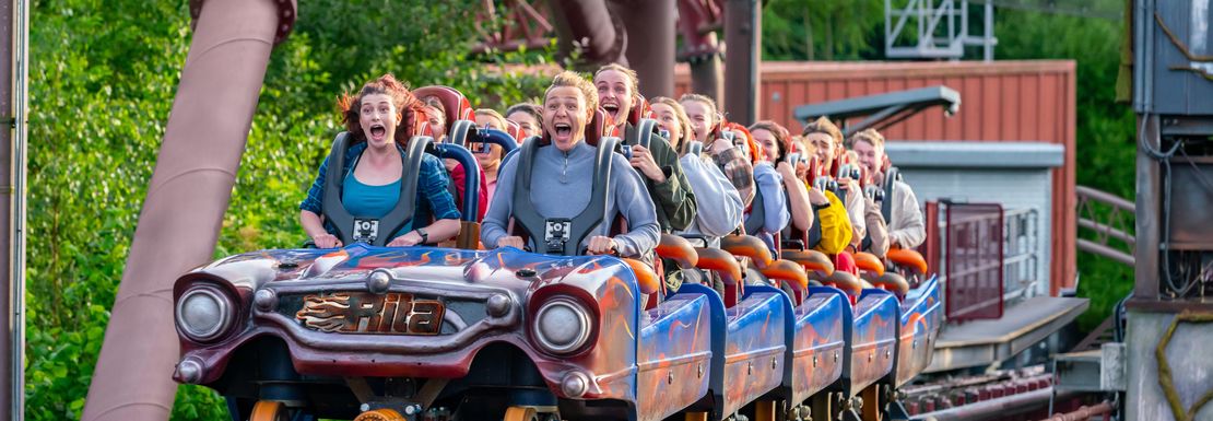 Roller coaster riders smile as a long set of cars rolls along the tracks