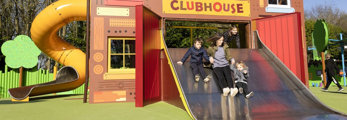 A mum and her children slide down a slide at the children's outdoor play area