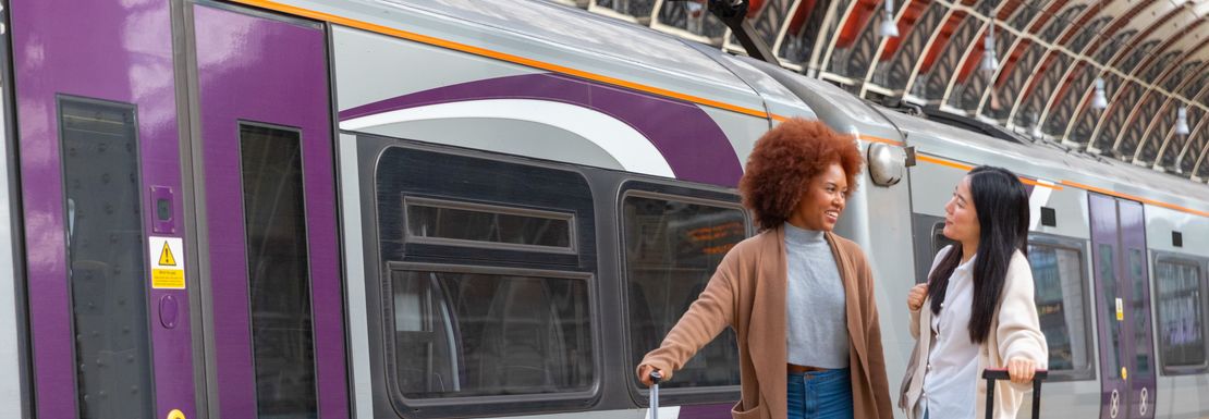 Two young ladies stand with their luggage outside of a Heathrow Express train
