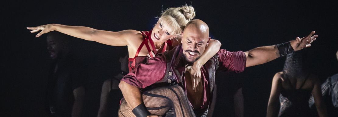 A couple dance together on stage with arms straight to the side