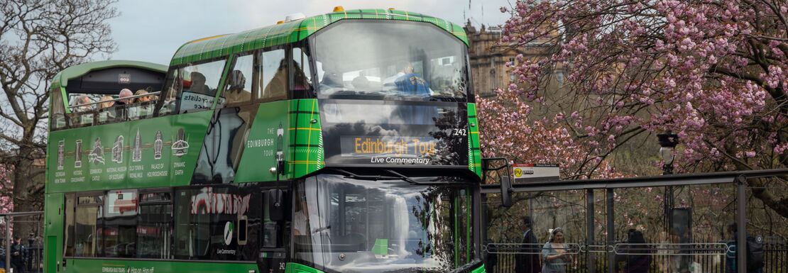 A green double decker bus driving on a city street, filled with passengers and adorned with advertisements.