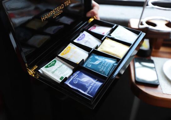 Person holding a black box filled with an assortment of delicious tea bag choices