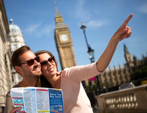 A couple point off to the distance whilst visiting London with Big Ben behind them