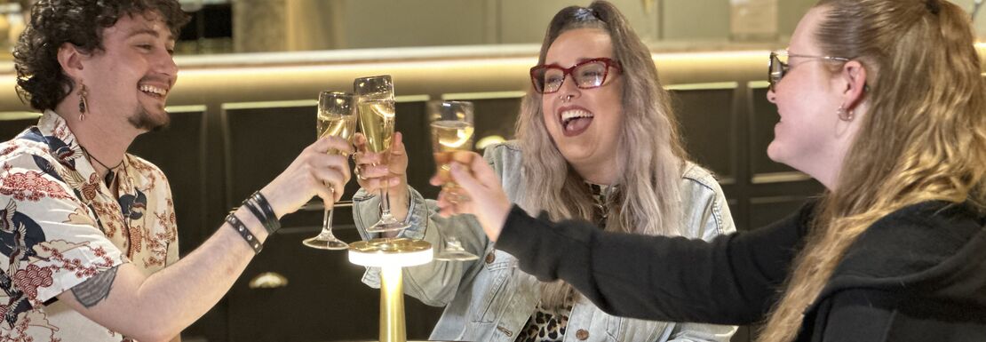 Friends sit around a table and cheers their glasses at Madame Tussauds Champagne Bar
