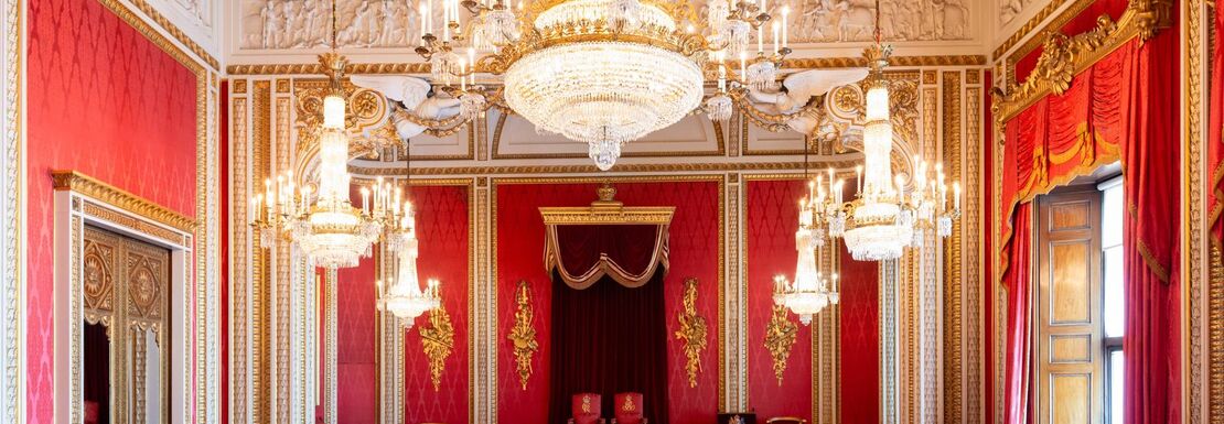 The throne room at Buckingham Palace with a large chandelier above the King's and Queen's thrones